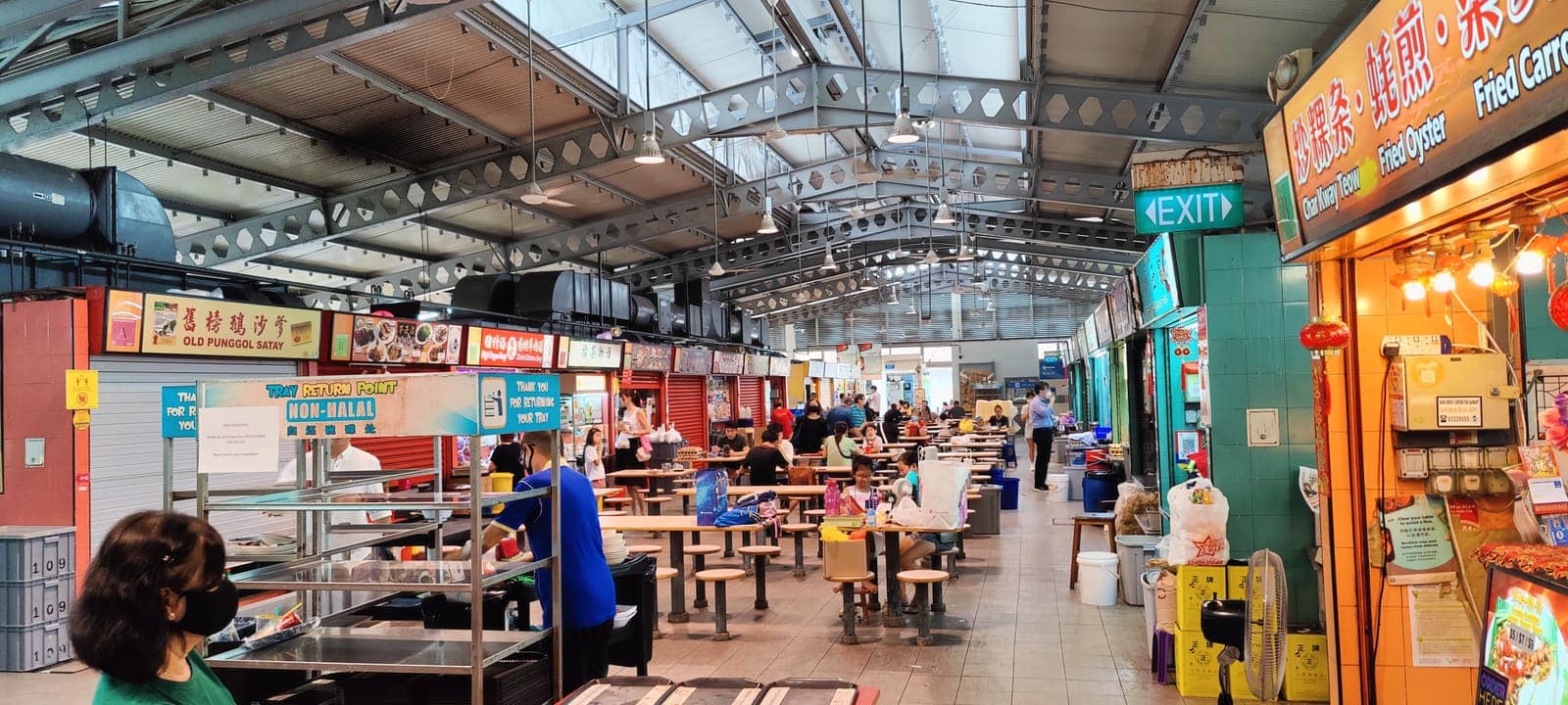 Stallholders and diners inside a Singapore hawker centre, stalls lining both sides of a covered hall